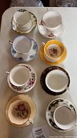 Top-down view of 8 assorted vintage porcelain tea cups and saucers, showing variety of floral patterns and gold trims.