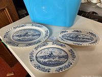 Three blue and white ceramic oval platters with windmill village scenes and floral borders placed on a white surface.
