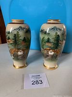 Full view of the pair of Chinese vases showing mirrored landscape paintings and golden rims and bases placed on a table.