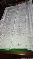 Full view of vintage linen table cloth with detailed pierced embroidery laid out flat on a table with 12 matching napkins on the side.