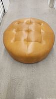 Front view of round tan leather ottoman on concrete floor