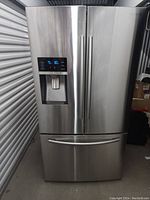 Front view of stainless steel French door refrigerator with external water and ice dispenser, digital display