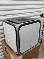 Cooker hood front, showing cubic design with white panels and gray rounded edges on a cardboard box.