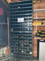 Front view of a tall dark gray steel storage cabinet with multiple compartments partially filled with hardware