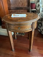 Full side view of the round side table showing drawer and four legs on wood floor.