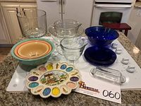 Full lot overview showing all glass bowls including clear and blue, ceramic Easter egg dish, and butter dish on stove surface.