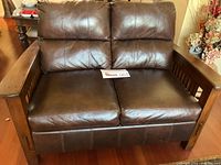 Front view of dark brown leather loveseat with wooden armrests and frame, showing the seat and back cushions
