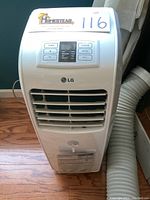 Front view of LG white portable air conditioner with flexible vent hose. Shows louvers and control panel below logo.