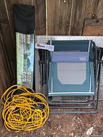 Photo showing folded Timber Ridge chaise lounge chair, Quick Shade Weekender Elite carrying bag for 10x10 ft instant canopy, and coiled yellow electric work lights with protective cages.