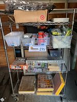 Photo showing full stainless steel rolling shelving unit loaded with plastic bins, cardboard box with black metal racks, and assorted hardware organizers on shelves.