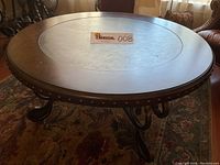 Angled side view of the round coffee table highlighting the rivet accents on the edge and ornate metal legs