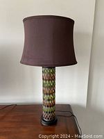 Full view of the lamp on a wooden surface showing the overall shape with the dark brown fabric shade and the colorful stained glass mosaic base.