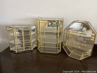 Three gold metal framed glass shelves with mirrored backs, bay window style, rectangular, and octagonal with etched rose design.