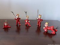 Front view of all five red ceramic pixie/devil figurines arranged in a row