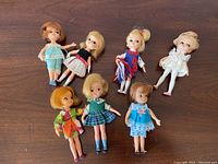 Seven vintage Darling dolls in original colorful outfits posed together on a wooden surface.