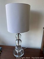 Full view of the modern acrylic table lamp with white cylindrical shade placed on a wooden surface.