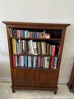 Front view of antique wooden bookcase filled with various books on three shelves, two-door cabinet at bottom closed.