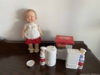 Full lot showing collectible doll, salt and pepper shakers, small saucer, and original salt & pepper box on wood surface.