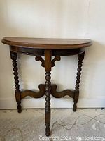 Front view of the demi lune table showing turned legs and a semi-circular top against a white wall.