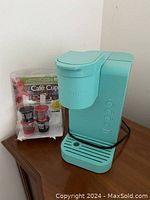 Full view of teal Keurig K-Espress coffee maker with 4 refillable pods included in packaging beside it on wooden surface.