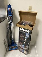 Full view of vacuum standing upright next to its original box and accessories.