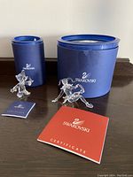Two Swarovski crystal figurines (Dopey and Jester), their certificates and original blue packaging cylindrical containers on dark wooden surface.