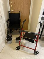 Black travel wheelchair and red walker side by side against door