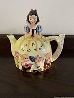 Front view of the Snow White musical teapot showing Snow White on the lid and three dwarfs on the body with musical notes and 'Hi Ho Hi Ho' text.