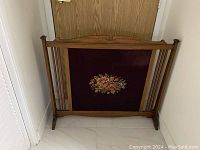 Front view of the wooden fireplace screen with floral petit point decoration on the fabric panel. Shows overall design and condition.