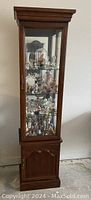 Full front view of tall wood and glass display cabinet with decorative molding and glass shelves filled with collectibles.