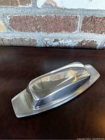 Butter dish with lid on, showing full shape and polish of stainless steel surface.