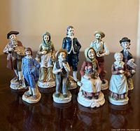 Nine Capodimonte porcelain figurines arranged on a surface in two rows, various characters with detailed painting and clothing, all standing on porcelain bases.