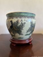 Front profile of the painted ceramic pot showing detailed crane, floral motifs, and Asian inscriptions on crackle-glaze surface, set on wooden stand.