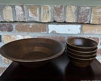 Stack of five smaller vermillion walnut bowls beside the large bowl on a dark surface against brick background.