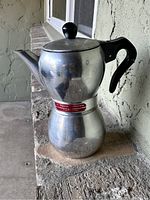 Front view of vintage Signora coffee percolator showing aluminum body, black handle, and label.
