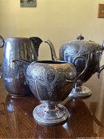Full view showing the three silver-plated items: teapot, creamer, and pitcher on wooden surface.