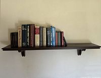 Full view of the wooden wall shelf mounted on the wall with books arranged from left to right.