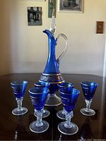 Full set including the cobalt blue crystal decanter with gilded band and stopper alongside six matching cobalt blue crystal glasses with clear stems.