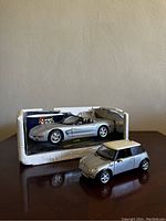 Photo of two small diecast model cars on a brown surface against a beige wall, one Corvette in original packaging and one Mini Cooper outside the box.