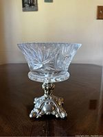 Front angled view of clear crystal dish with cut leaf and starburst design on ornate brass base