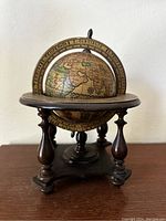 Front view of vintage wooden globe showing continents, zodiac signs, and inscriptions with wooden stand.