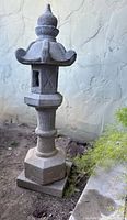 Front view of a vintage Kasuga granite lantern with detailed top finial and open window with 'X' carving on the body.