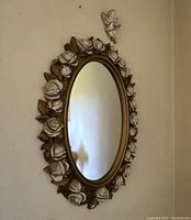 Oval mirror with carved wooden roses on the frame hanging on wall with angel decoration above