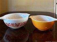 Two Pyrex nesting bowls side by side, one solid yellow and one white with orange and red pattern