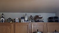 Wide shot of 7 nautical decorative items including lighthouse lamps and birdhouses on top of cabinets.