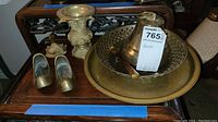 Collection of brass items including the vase, bell, two shoe-shaped figurines, and brass trays laid out on a wooden table