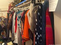 Long rack of women's clothing including sweaters, tops, pants, and a fur jacket on hangers.