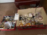 Two holiday-patterned tin boxes filled with assorted costume jewelry pieces