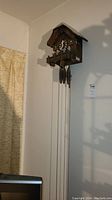 Cuckoo clock mounted high on a wall, showing full length with chains and weights hanging.