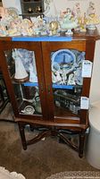 Front view of the vintage wooden display cabinet filled with collectible figurines (figurines not included in the lot). The cabinet stands on curved legs and has clear glass panels with a warm wood finish.